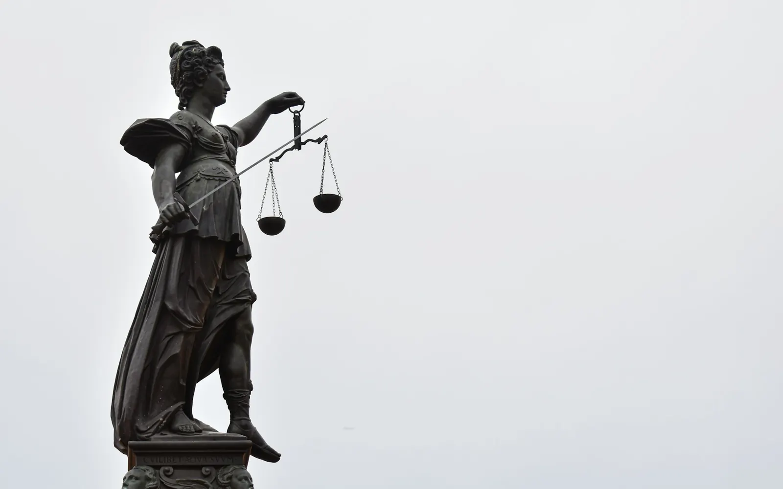Statue of Lady Justice holding scales against an overcast sky